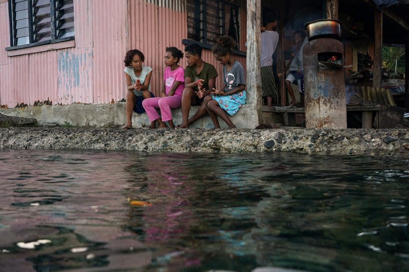 Village children pass the time in front of a home next to a flooding sea wall at high tide in Serua Village, Fiji, July 15, 2022. As the community runs out of ways to adapt to the rising Pacific Ocean, the 80 villagers face the painful decision whether to move. (CNS photo/Loren Elliott, Reuters)