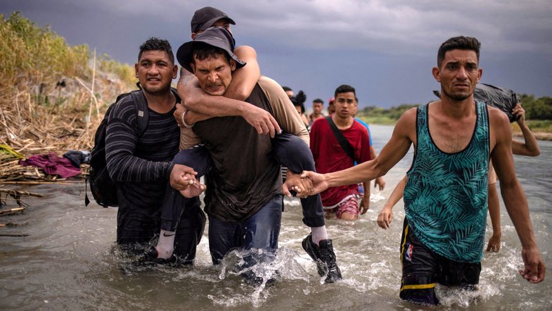 Douglas and David assist Leon, a migrant from Venezuela, as he carries his handicapped cousin Luis Sept. 15, 2023, after they waded across the Rio Grande from Mexico to the United States. The migrants were searching for an entry point past razor wire in Eagle Pass, Texas. (OSV News/Adrees Latif, Reuters)