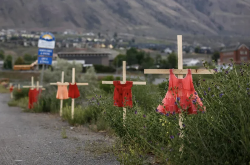 Children's red dresses are staked along a highway near the former Kamloops Indian Residential School where flowers and cards have been left as part of a makeshift memorial created in response to media reports that the "remains" of 215 children have been discovered buried near the facility, in Kamloops, British Columbia, Canada, on June 2, 2021. (Cole Burston/AFP via Getty Images)