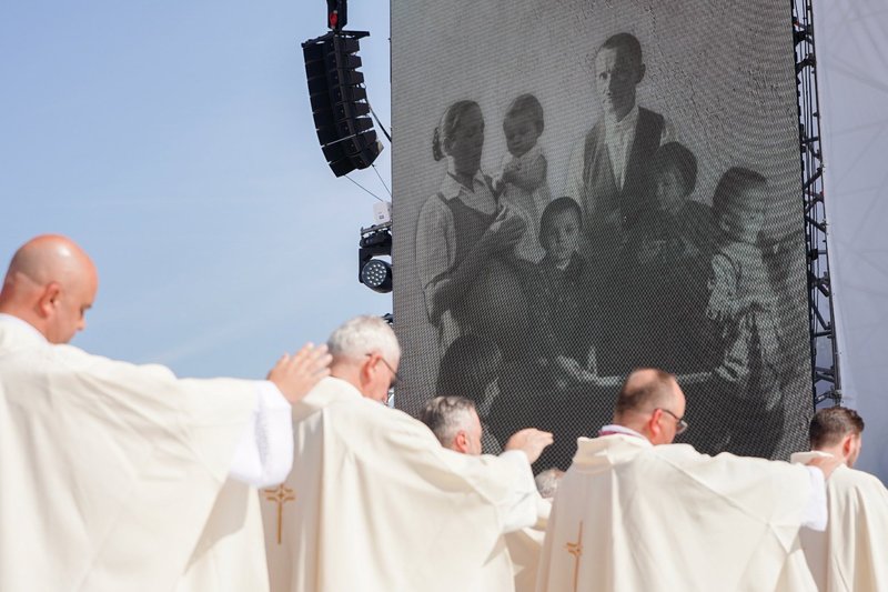 Priests raise their hands during the consecration of the Eucharist at the Sept. 10 beatification Mass of the Ulma family in Markowa, Poland. In the background is a photo of the Ulmas taken shortly before their death, in which Wiktoria is seen visibly pregnant. (CNS/Justyna Galant)