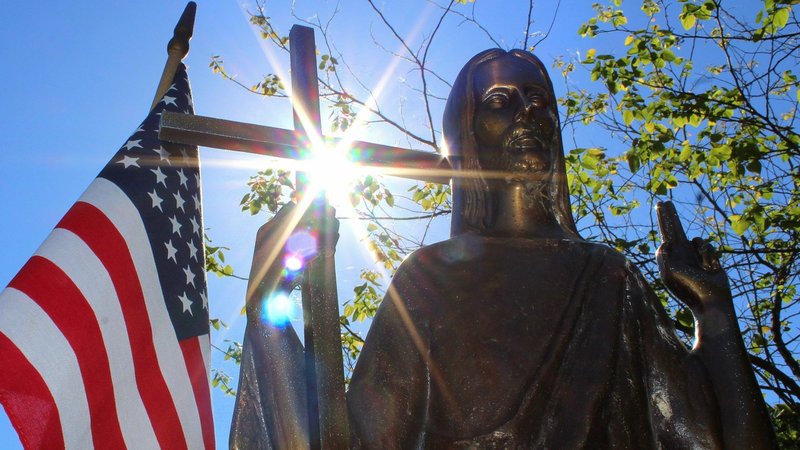 Sun shines through a statue of Christ on a grave marker alongside an American flag at St. Mary Catholic Cemetery in Appleton, Wis., in this 2018 photo. (OSV News photo/Bradley Birkholz)