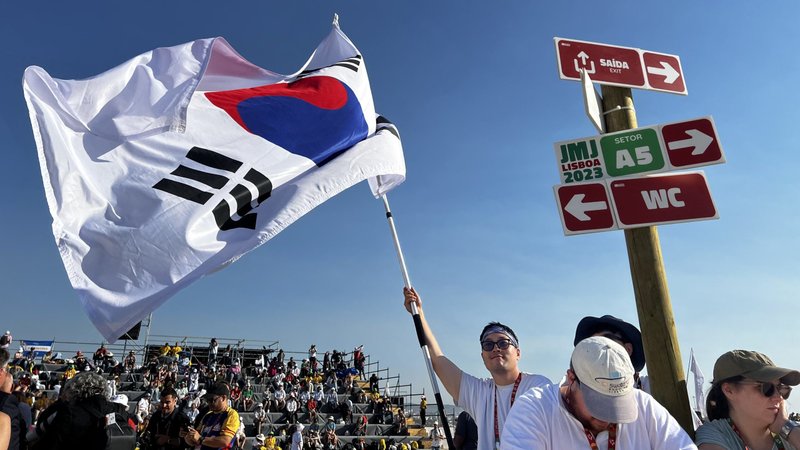 A young man from South Korea waves his country's flag before Pope Francis arrives for the closing Mass of World Youth Day at Tejo Park in Lisbon, Portugal, Aug. 6, 2023. At the end of Mass, the pope announced the next WYD will be held in Seoul, South Korea, in 2027. (CNS photo/Lola Gomez)