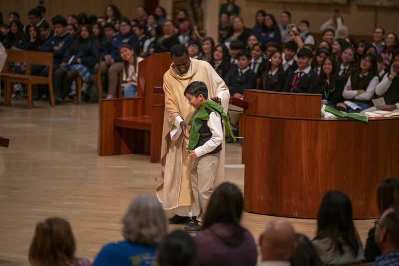Father Frederick Byaruhanga, a priest originally from the Diocese of Kabale in Uganda and now a chaplain for the VA Greater Los Angeles, has a student help him during his homily for the annual Missionary Childhood Association Youth Appreciation Mass on Oct. 16. (John Rueda)