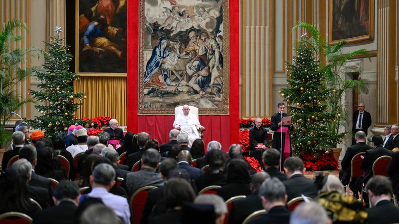 Pope Francis listens as Msgr. Filippo Ciampanelli, an aide, reads the pope's prepared text to ambassadors and diplomats accredited to the Holy See during their annual meeting in the Hall of Blessing in the Apostolic Palace at the Vatican Jan. 9, 2025. Pope Francis told the diplomats that he had a cold and asked the aide to read his speech. (CNS photo/Vatican Media)