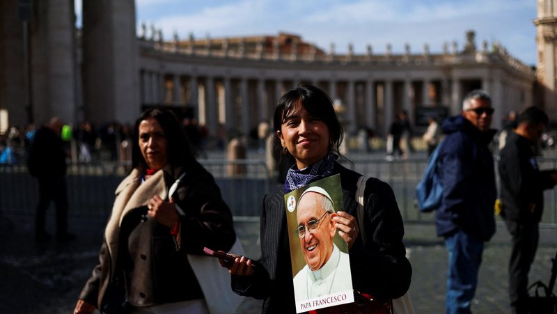A woman smiles as she holds an image of Pope Francis in St. Peter's Square at the Vatican Feb. 26, 2025, as he continues his treatment for double pneumonia at Rome's Gemelli Hospital. (OSV News/Claudia Greco, Reuters)