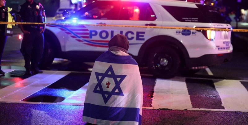 A man, with an Israeli flag with a cross in the center, kneels next to emergency personnel early May 22, 2025, as they work at the site where, according to the U.S. Department of Homeland Security, two Israeli Embassy staff were shot dead near the Capital Jewish Museum in Washington late May 21. The American Jewish Committee was hosting an evening event at the museum. (OSV News photo/Jonathan Ernst, Reuters)