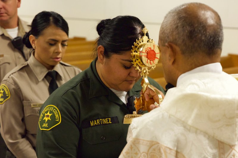 Msgr. Anthony Figueiredo holds the reliquary with St. Carlo Acutis’ pericardium to a sheriff's deputy's forehead during the saint's relic visit to LA Men’s Central Jail on Oct. 20. (Reese Cuevas)
