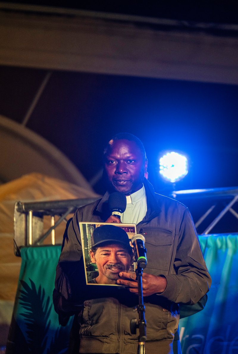 Father John Kyebasuuta, pastor of St. Elizabeth of Hungary Catholic Church in Altadena, holds a picture of Eaton Fire victim Victor Shaw at a Jan. 7 interfaith vigil marking one year since the fire. (Juanito Holandez Jr.)