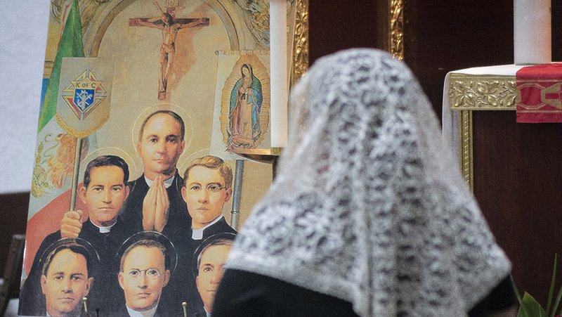 Parishioner Esther de la Rosa, right, prays during a Mass for peace in Mexico on Feb. 24 at Our Lady of the Rosary of Talpa Church in Boyle Heights, where the relics of six Mexican martyrs were on display. A poster of the martyrs is on the left. (Juanito Holandez Jr.)