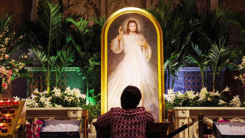 A woman kneels in prayer in front of a “Divine Mercy” painting of Jesus Christ inside St. Patrick’s Cathedral in New York City April 13. (OSV News/Shannon Stapleton, Reuters)