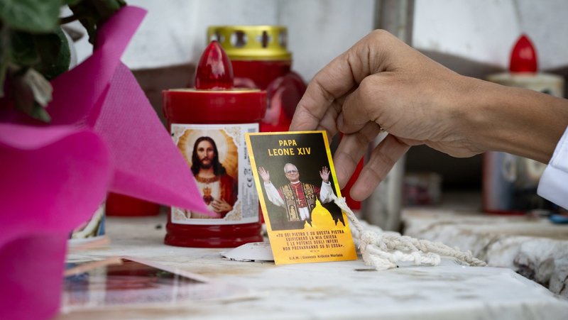 A woman touches some devotional items placed next to a statue of St. John Paul II Oct. 14, 2026, in front of Rome's Gemelli hospital where Pope Leo XIV is recovering from surgery during which doctors removed his lower right lung to treat a cancerous tumor. (CNS photo/Cristian Gennari)