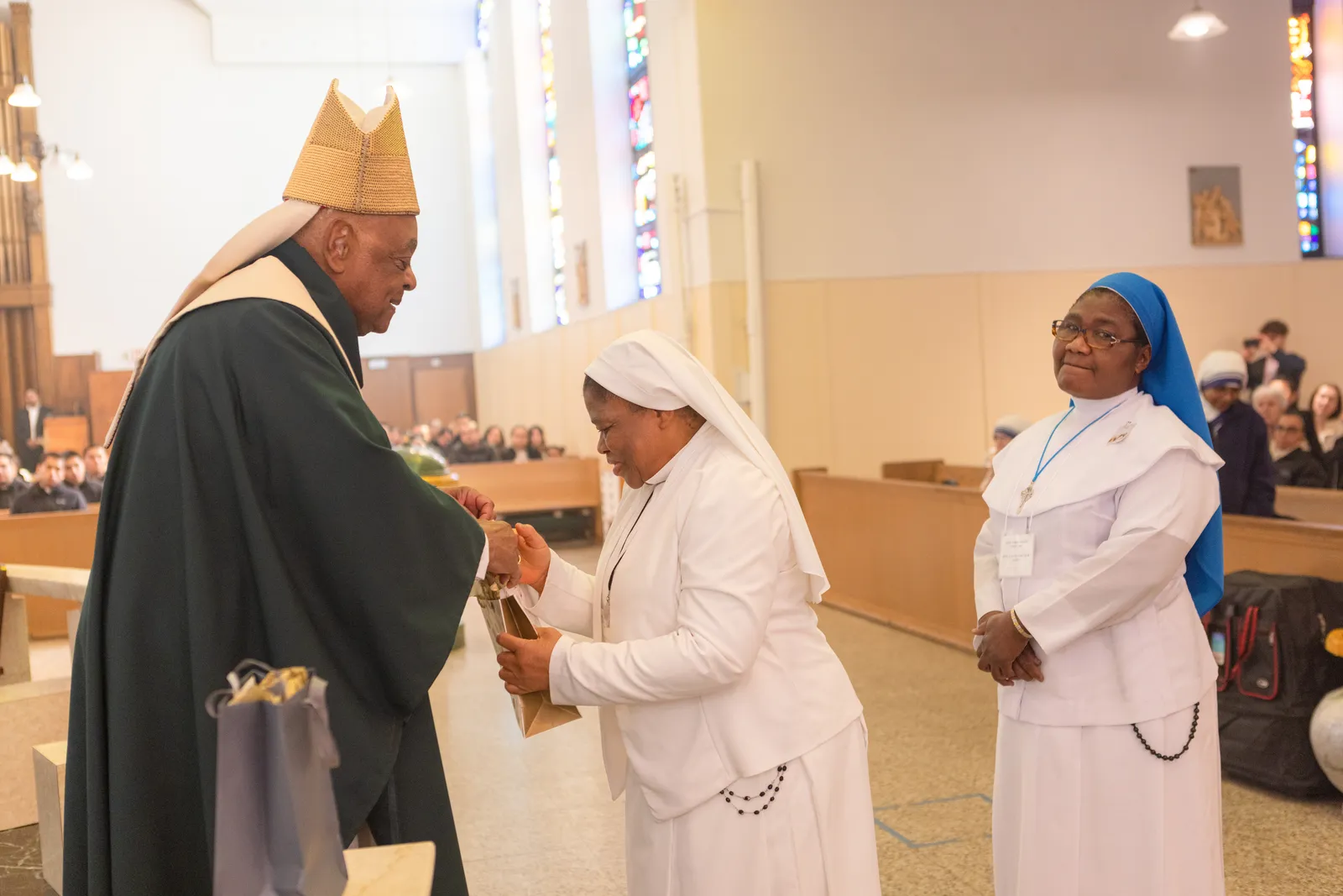 After celebrating a Mass on Feb. 9 at St. Bernard of Clairvaux Church in Riverdale Park, Maryland, to honor men and women in consecrated life serving in The Roman Catholic Archdiocese of Washington who are celebrating milestone anniversaries, Cardinal Wilton Gregory presents a gift to Sister Joanna Okereke of the Handmaids of the Holy Child Jesus who is marking her 40th anniversary in religious life. At right is Sister Ibeh Miriam Mercy of the Daughters of Divine Love who is also marking her 40th anniversary. (Catholic Standard photo by Rachel Lincoln)