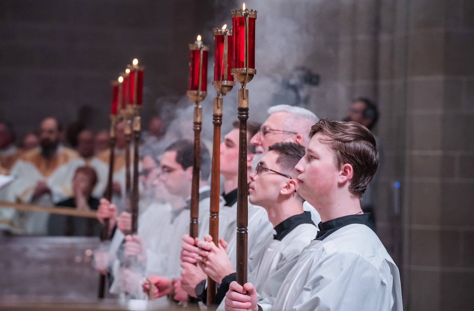 Altar servers hold candles as incense billows during the Chrism Mass.