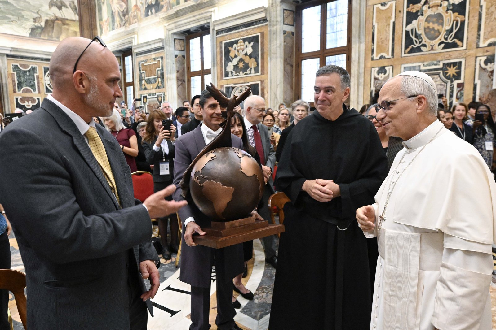 El Papa León XIV recibe la escultura "La paz sea con todos ustedes" del artista Timothy Schmalz, a la izquierda, mientras el padre Joseph L. Farrell, prior general de la orden agustiniana, observa durante una audiencia en el Vaticano el 2 de octubre de 2025. (Foto CNS/Vatican Media)