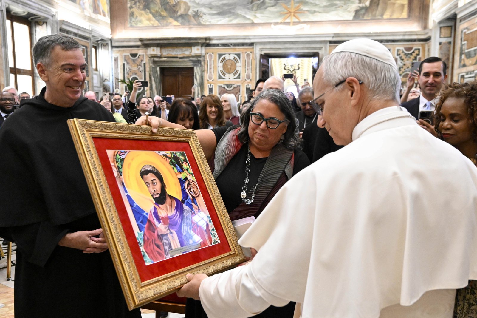 El Papa León XIV recibe una copia de la pintura de San Agustín llamada "Una aquilegia improbable: santo de Hipona del norte de África" de Michele R. Pistone, fundadora y directora de la facultad del Instituto Madre Cabrini sobre Inmigración de la Universidad de Villanova, durante una audiencia en el Vaticano el 2 de octubre de 2025. El padre Joseph L. Farrell, prior general de la orden agustiniana, observa. (Foto CNS/Vatican Media)
