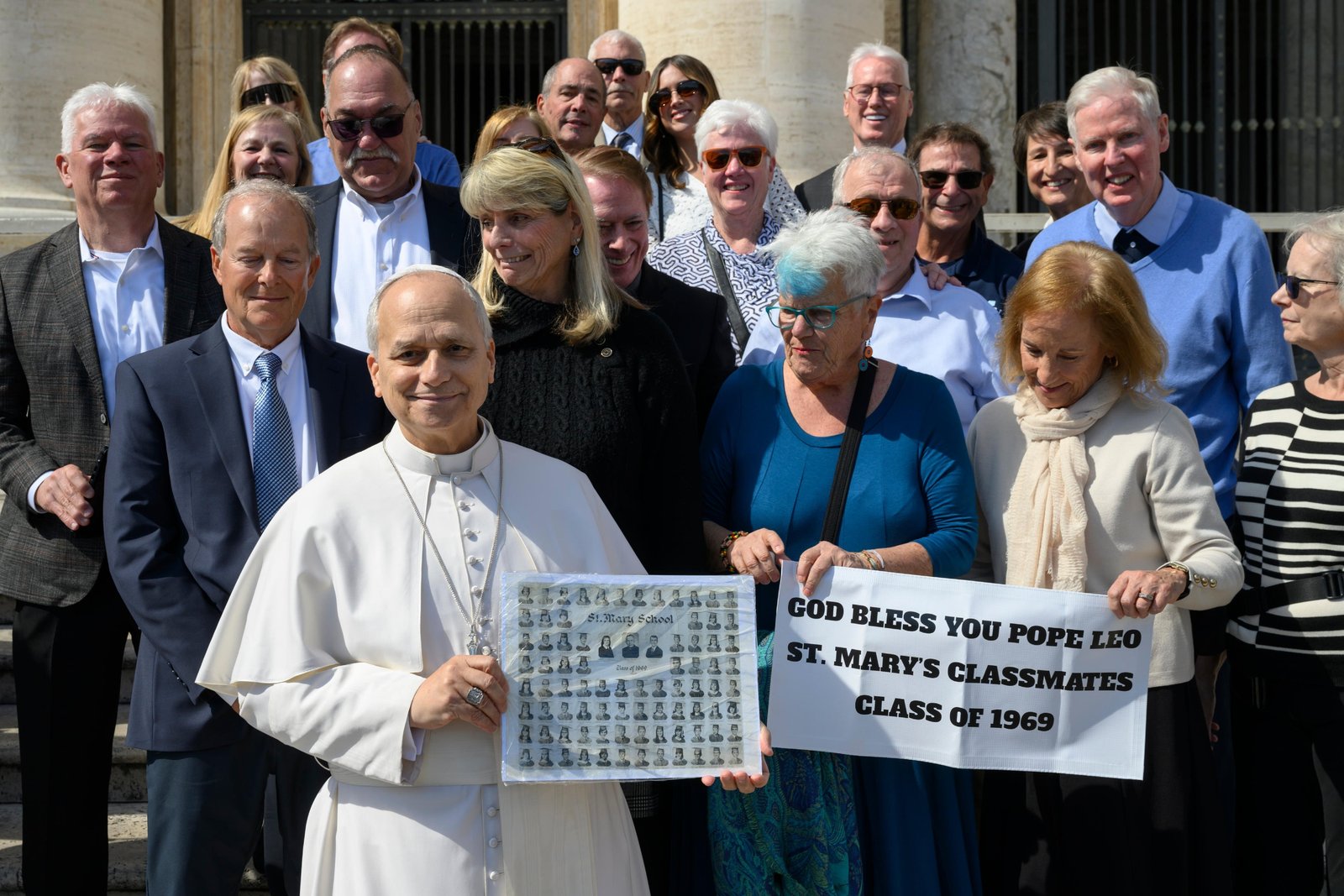 Pope Leo XIV poses with former classmates who graduated from the lower school of St. Mary of the Assumption in Chicago in 1969 after the general audience in St. Peter's Square at the Vatican March 18, 2026. He is holding their eighth-grade graduation class photo. (CNS photo/Vatican Media)