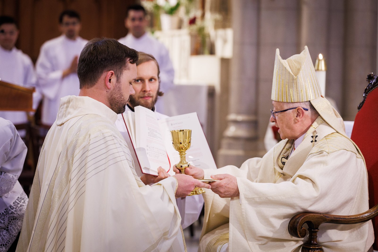 Fr. Ippel (left) kneels in front of Cardinal Blase J. Cupich during his ordination on June 14, 2025.