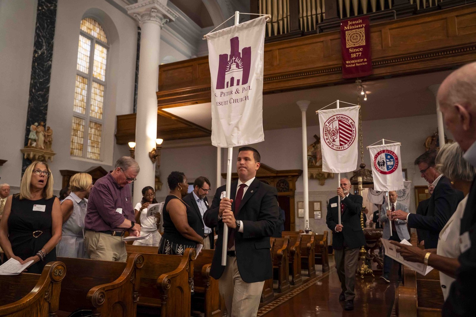 Representantes de diversos ministerios jesuitas del área de Detroit llevan pancartas que representan los apostolados para dar inicio a la misa en la fiesta de San Ignacio de Loyola, fundador de la Compañía de Jesús.