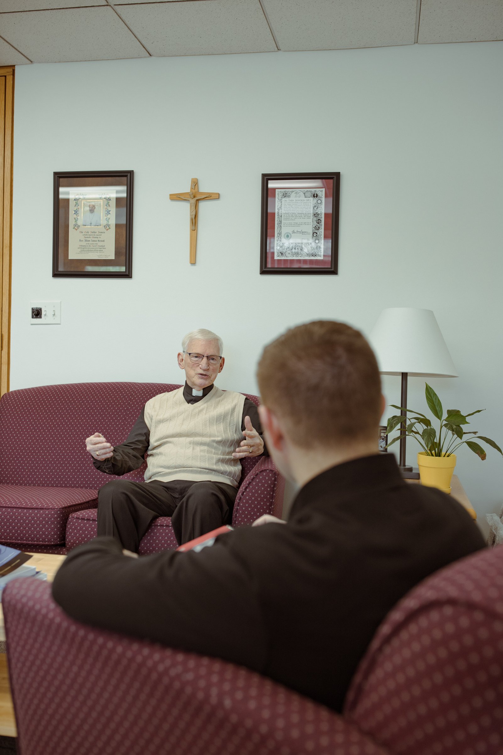 Padre Nowak, a la derecha, entrevista a Mons. McEnhill para una tarea de clase. Padre Nowak está tomando cursos en línea para obtener una maestría en administración de empresas de la Universidad de Bismarck en Dakota del Norte.