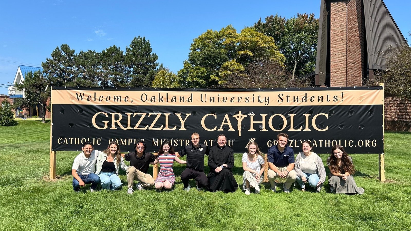 Fr. Steven Mateja, center, poses with Oakland University students in front a sign for Grizzly Catholic at St. John Fisher Chapel University Parish in Auburn Hills. (Courtesy of St. John Fisher Chapel University Parish)