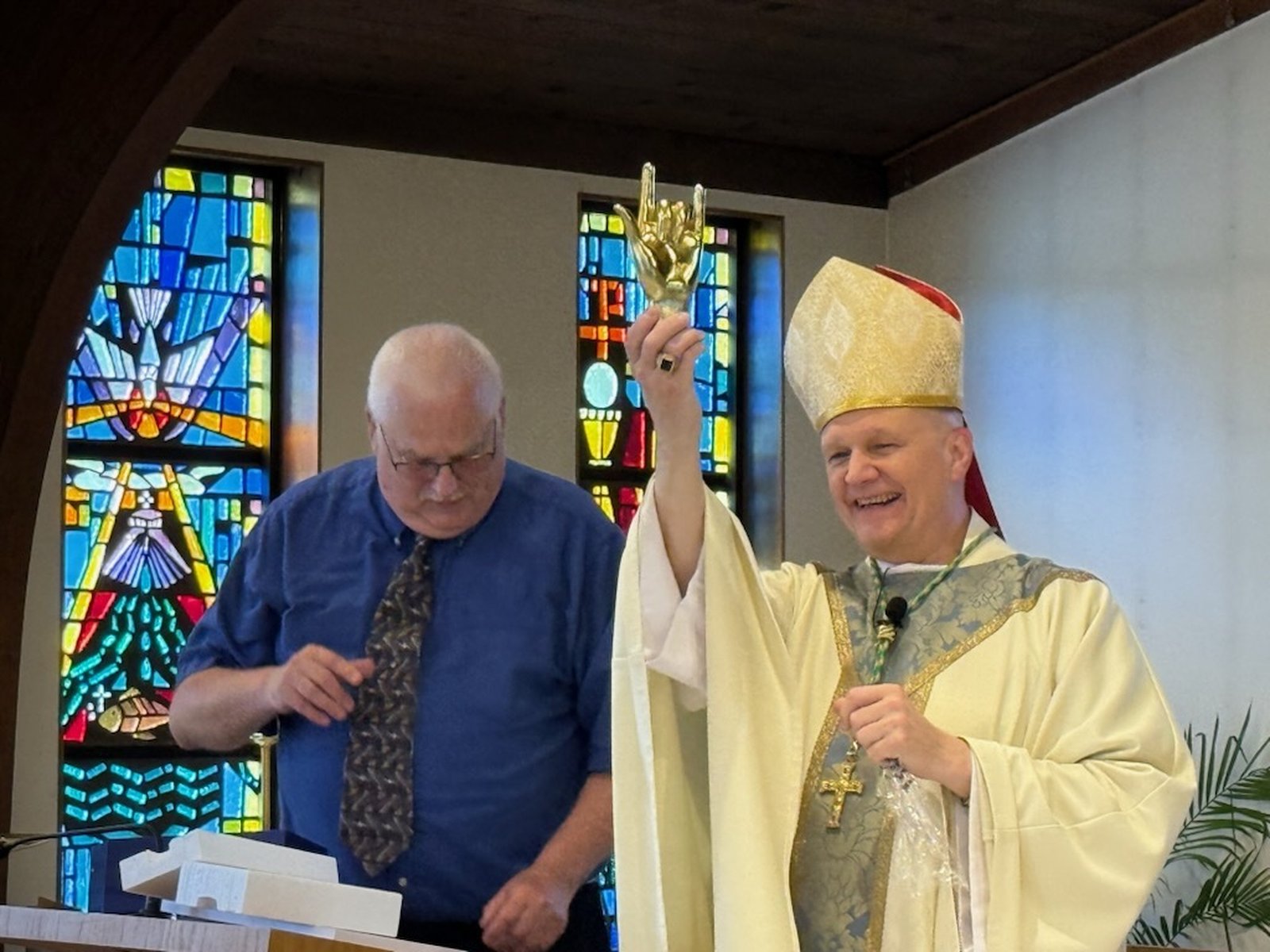 Archbishop Weisenburger holds up a small statue given to him by members of the Deaf Catholic community, a small statue of a hand signing "I love you."