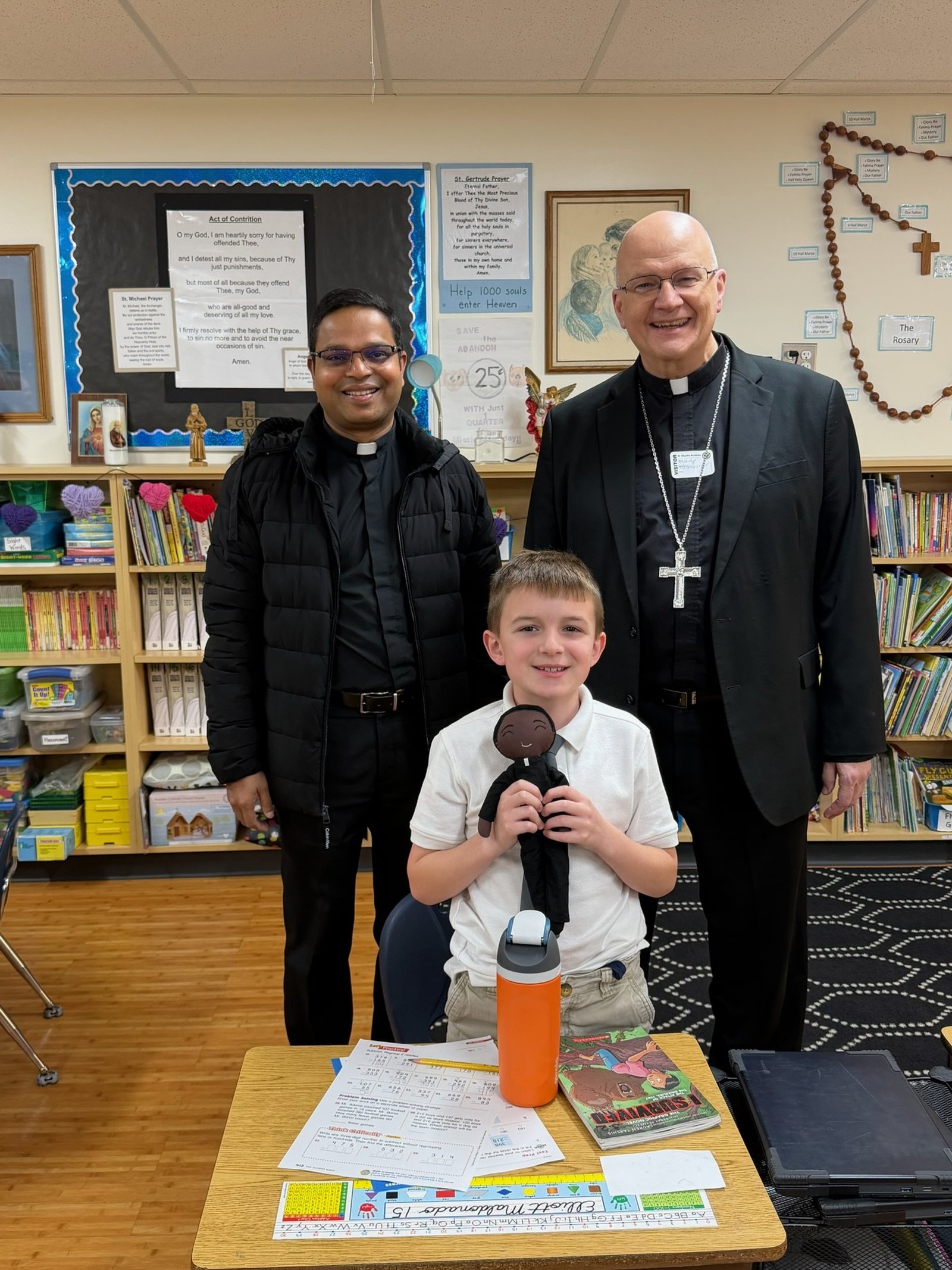 A young man shows his stuffed figure representing his pastor, Fr. Henry Rebello, left, along with Archbishop Weisenburger.