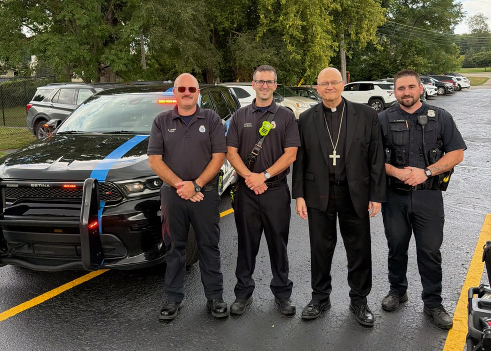 Archbishop Weisenburger poses alongside representatives from the local fire department and police department, who showed up to provide security for the huge parish picnic after Mass. Many of the parish school's 400 students were present.