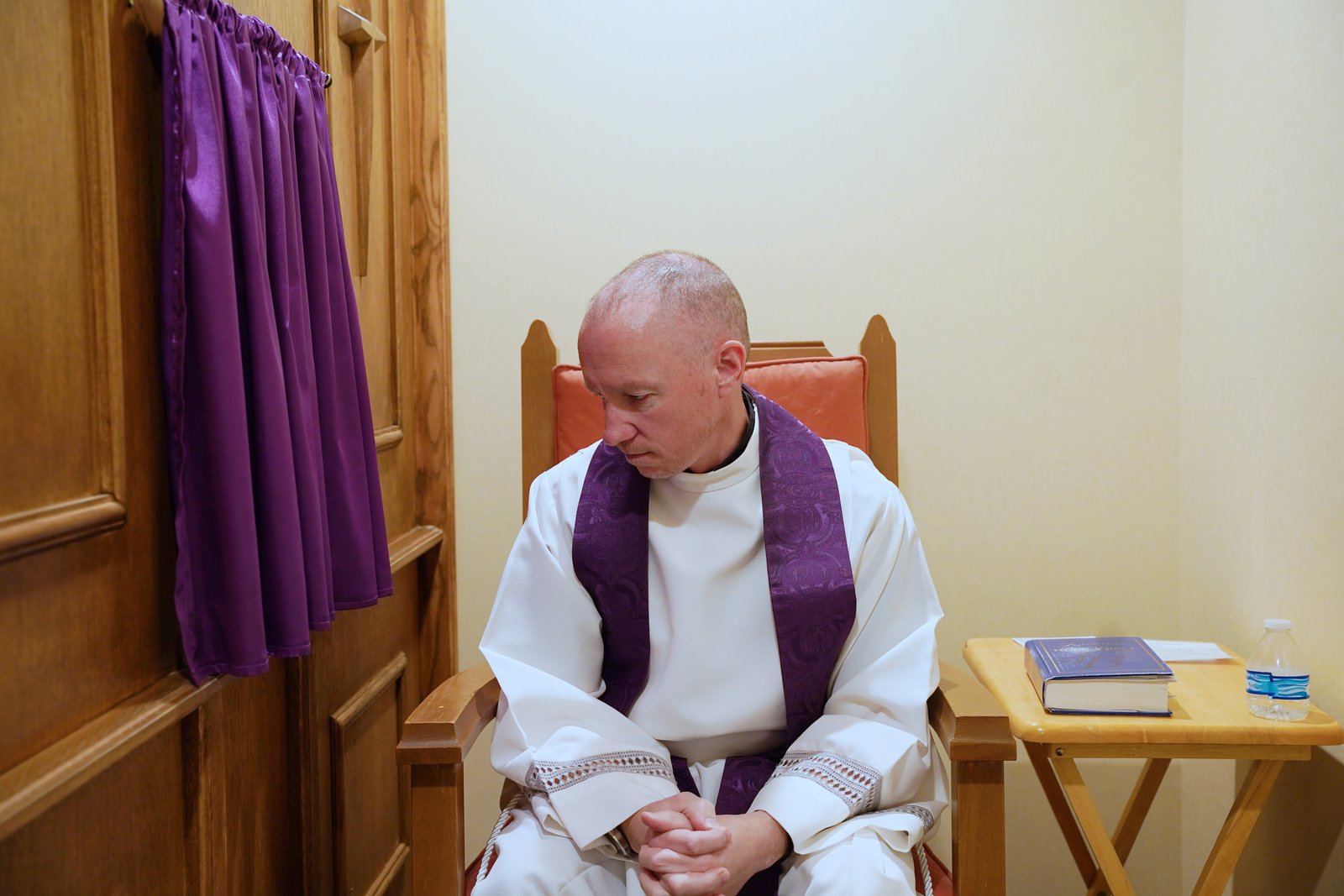 Fr. Andrew Dawson sits next to the new confessional screen at Prince of Peace Parish in West Bloomfield in this staged photo.