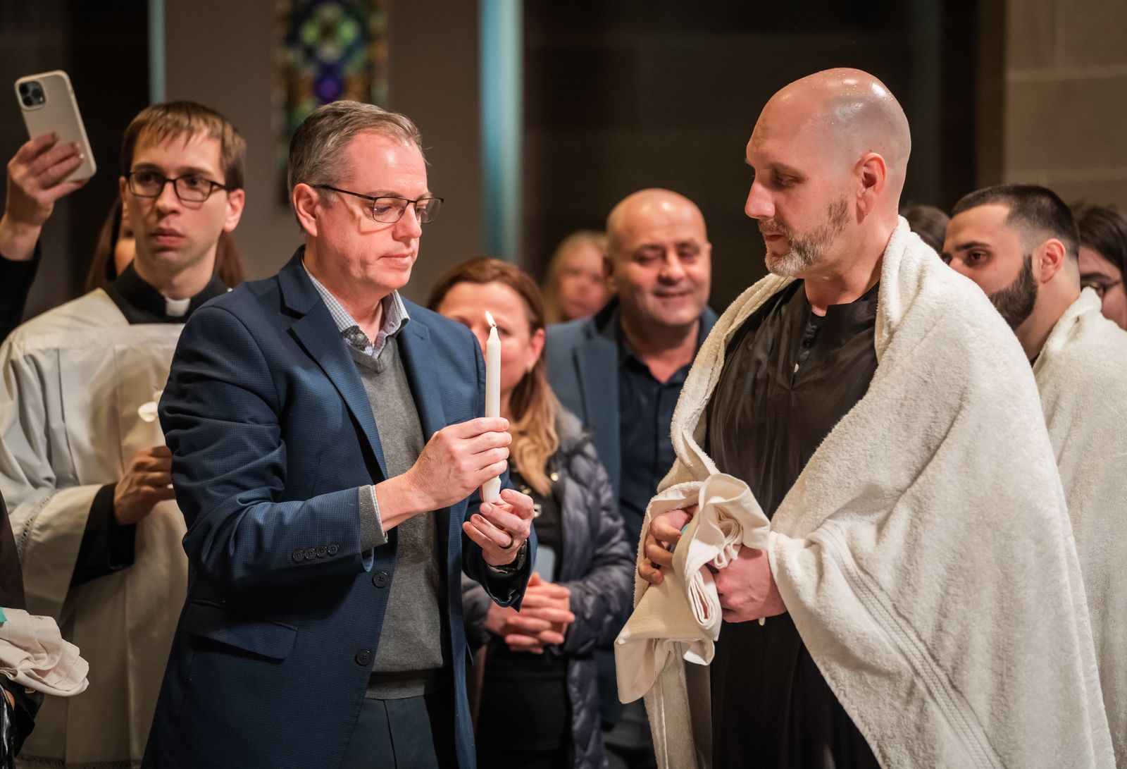 Brian Mull receives the "light of Christ" from his sponsor and co-worker, Jerry McElhone, left, after his baptism. Mull said it was special to enter the Catholic faith alongside his co-workers, receiving baptism, confirmation and first Communion from his boss, Archbishop Vigneron.