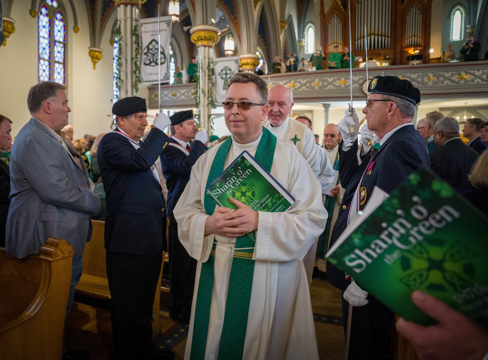 Fr. Brendan McCarrick, SAC, pastor of St. Vincent Pallotti Parish in Wyandotte, holds a "Sharin' o' the Green" Mass booklet as he processes into the church, flanked by members of the Knights of Columbus honor guard.