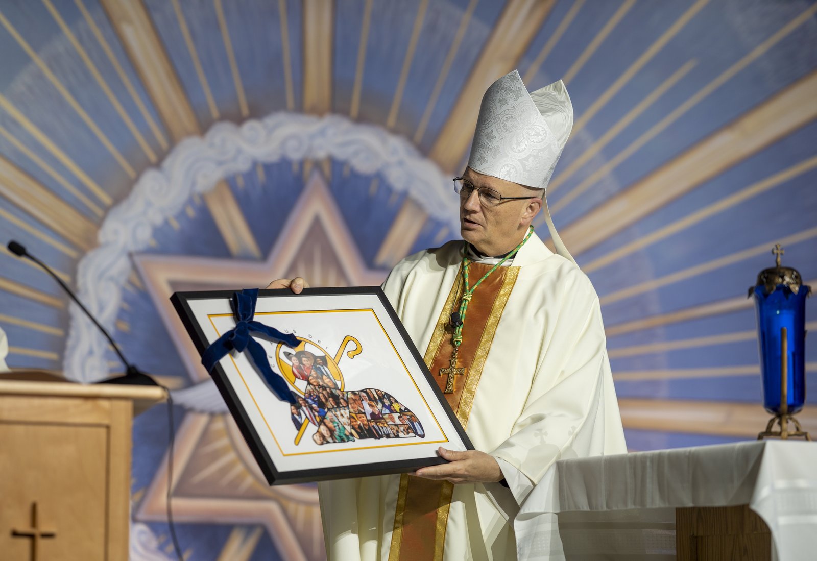 Archbishop Weisenburger holds a portrait featuring an image of a lamb made up of a collage of smaller portraits of students from across the Archdiocese of Detroit, inspired by the archbishop's episcopal coat of arms. The portrait was a gift presented to the archbishop by the archdiocesan Department of Catholic Schools.