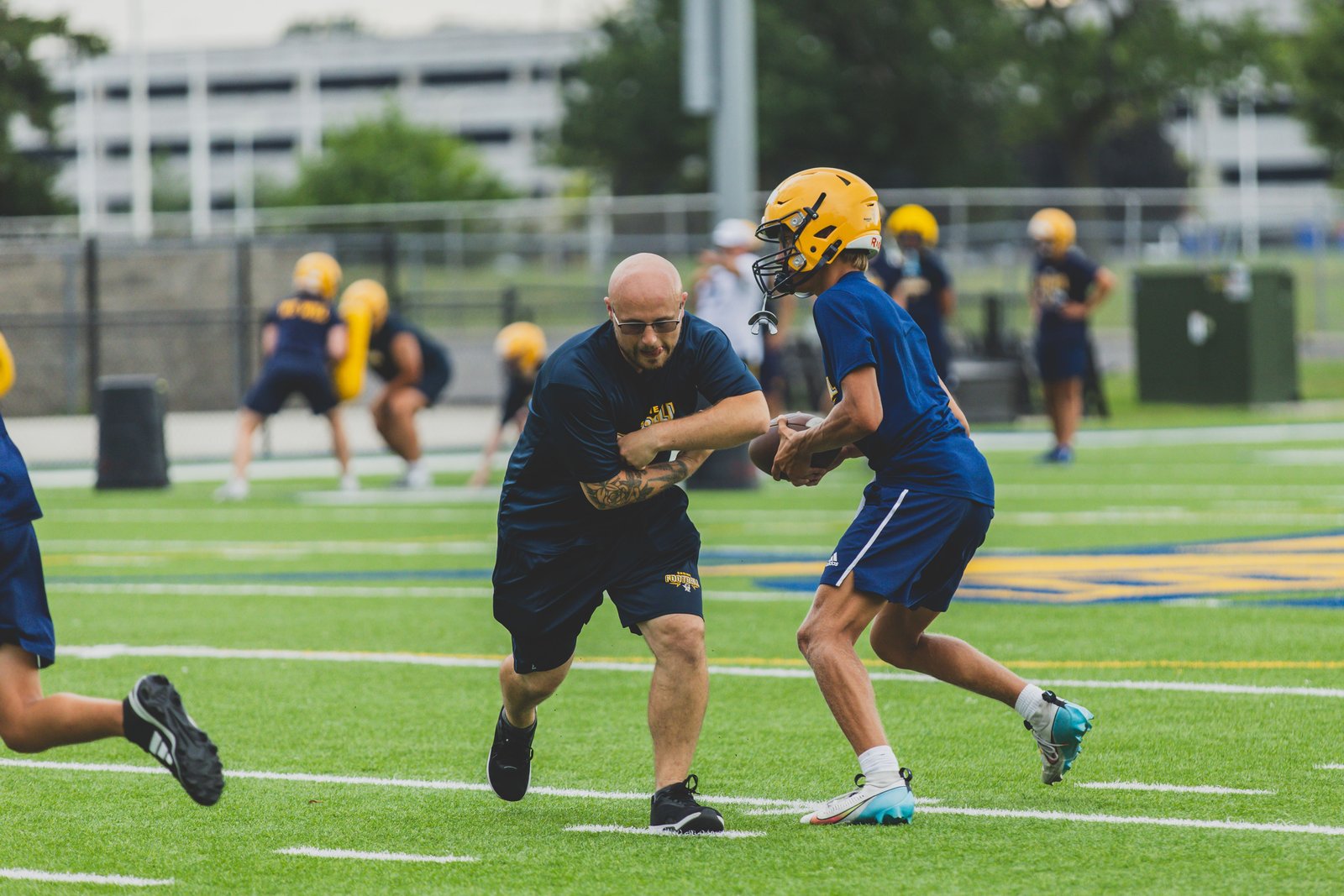 Chris Kelly, who was a running back for Shrine High School and later Hope College, jumps in a drill on the first day of practice, preparing to take a handoff from quarterback Jack Tisko. (Photo by Katrina Shammami | Special to Detroit Catholic)