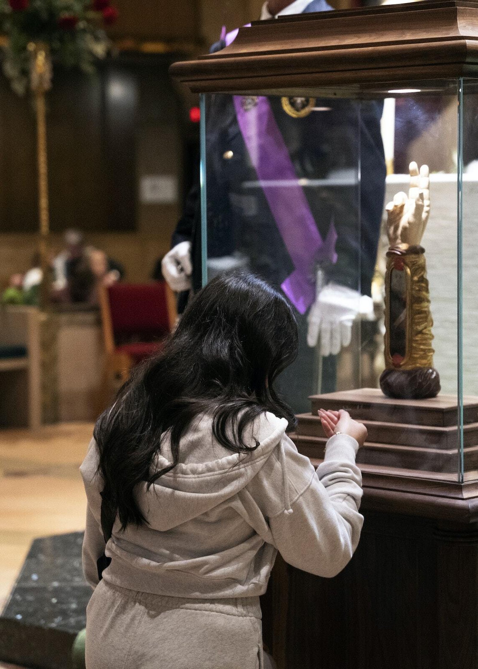 Una mujer se arrodilla en oración ante la reliquia de San Judas, que se encuentra en un gran relicario que simula el brazo derecho del santo, levantado en señal de bendición.