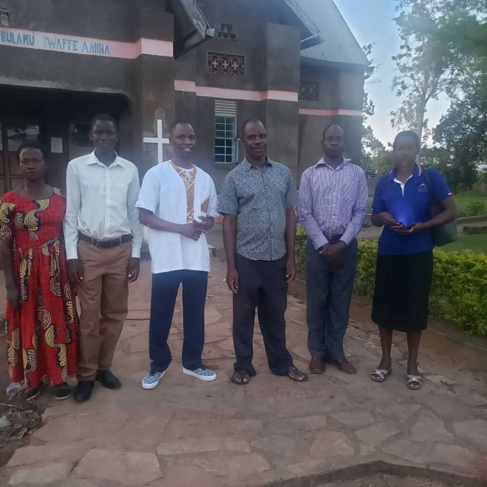 Joseph Kirembwe, third from left, joins his brother, Fr. Denis Ssebuggwawo, third from right, and siblings after Mass in front of Holy Family Namayumba Catholic Parish in the Wakiso District, Kampala Archdiocese of Uganda. Fr. Denis serves as pastor of Holy Family. (Courtesy of Joseph Kirembwe)