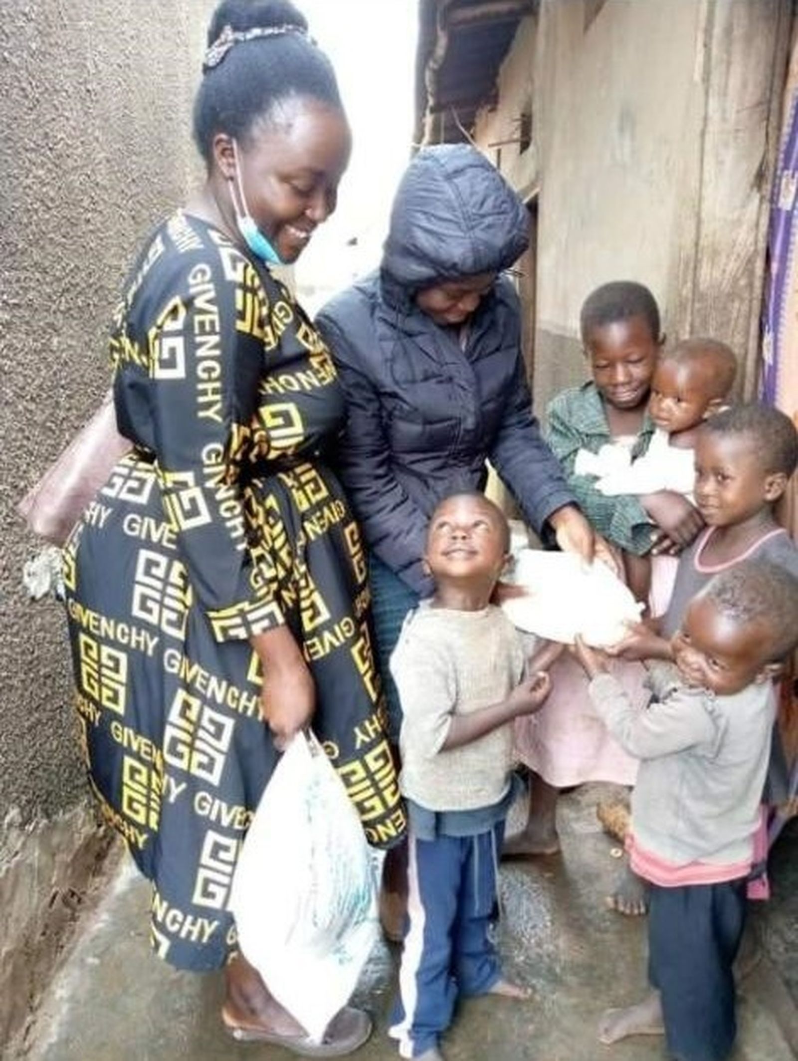 Ida Nakalembe, left, and Ruth Lunkuse of Ria Child Care & Women Empowerment Ministries, give clothing and school supplies to first-grader Marvin Lubowa (looking up) and other children. (Courtesy of Joseph Kirembwe)
