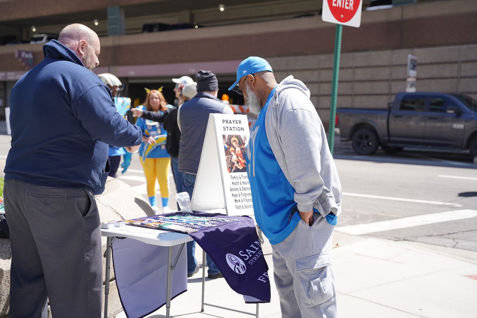 Un aficionado de los Detroit Lions observa la mesa de Evangelización en la Calle St. Paul, que tiene rosarios, medallas milagrosas y tarjetas de oración. Los evangelizadores estaban disponibles para hablar sobre Jesús, el catolicismo y hacer amistad con los transeúntes.