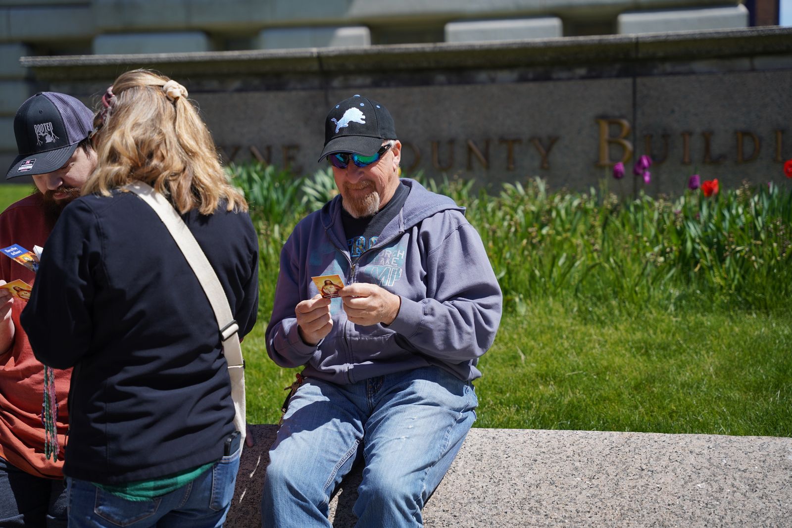 Beth Schuele de St. Paul Street Evangelization entrega una tarjeta de oración a un aficionado de los Detroit Lions que está sentado frente al antiguo Edificio Wayne County en el día del draft.