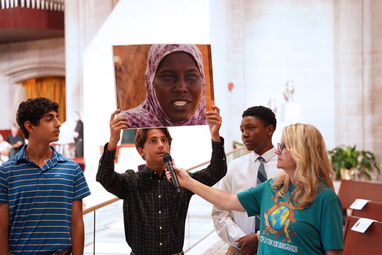Young people hold photos of migrants and read their testimonies before Mass begins.