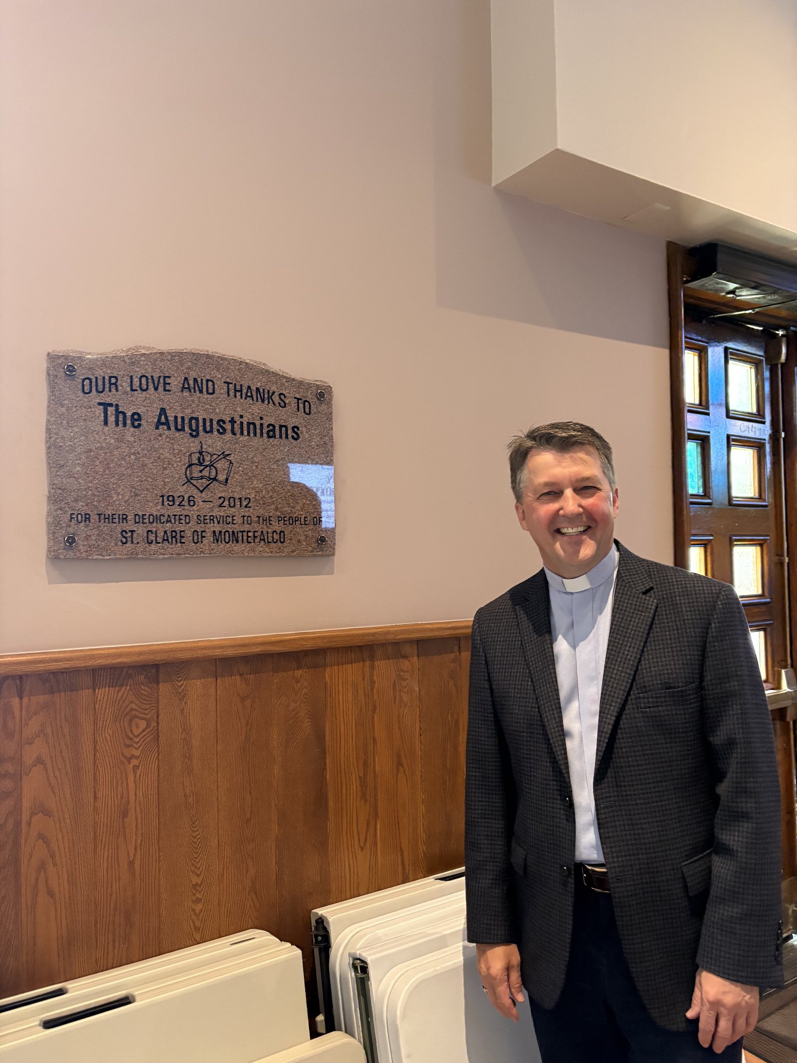 El P. Andrew Kowalczyk, CSMA, se encuentra junto a una placa que conmemora los muchos años de servicio de los agustinos en la Parroquia Santa Clara de Montefalco. La placa que conmemora la ordenación diaconal del papa León será instalada junto a la placa de los agustinos.