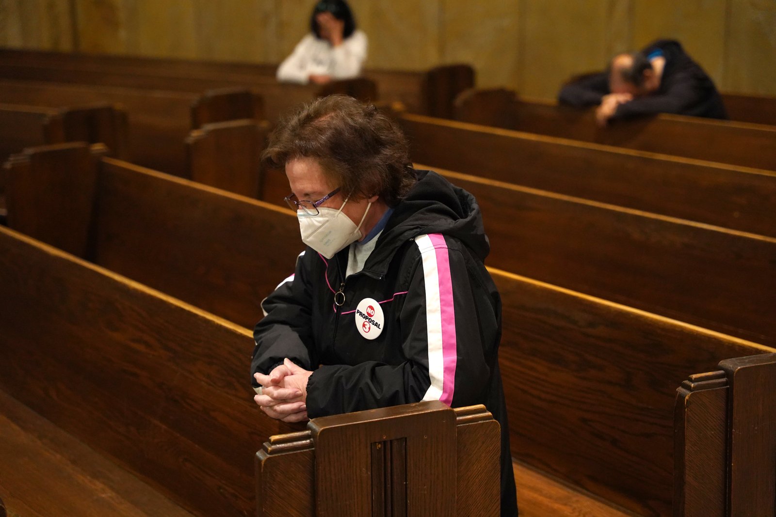 A woman wearing a "No on Proposal 3" button bows her head in prayer at the National Shrine of the Little Flower Basilica in Royal Oak.