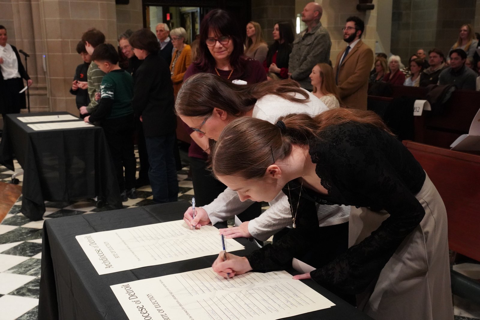 Catecúmenos firman su nombre en el Libro de los Elegidos antes de avanzar en procesión hacia el santuario de la catedral, donde se colocaron ante el arzobispo Weisenburger en un antiguo rito, como preparación para su plena incorporación a la Iglesia esta Pascua.