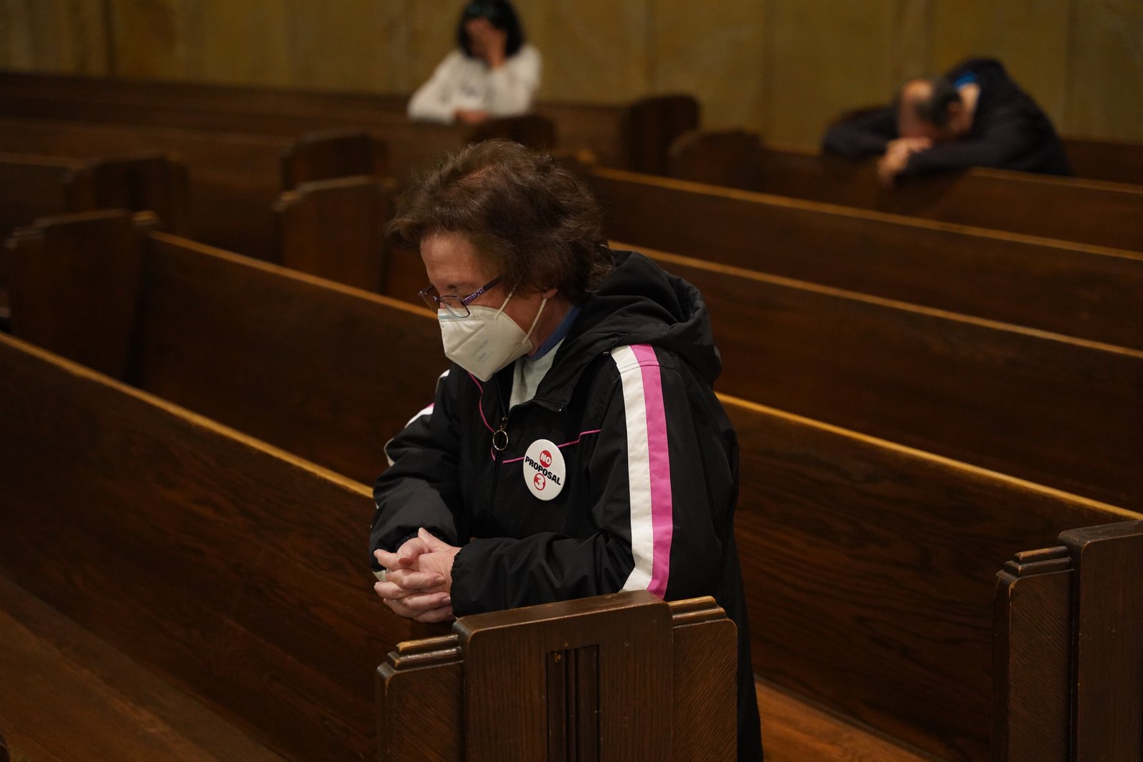 Una mujer que lleva un botón que dice "No a la Propuesta 3" inclina la cabeza en oración en el Santuario Nacional de la Basílica de la Little Flower en Royal Oak.