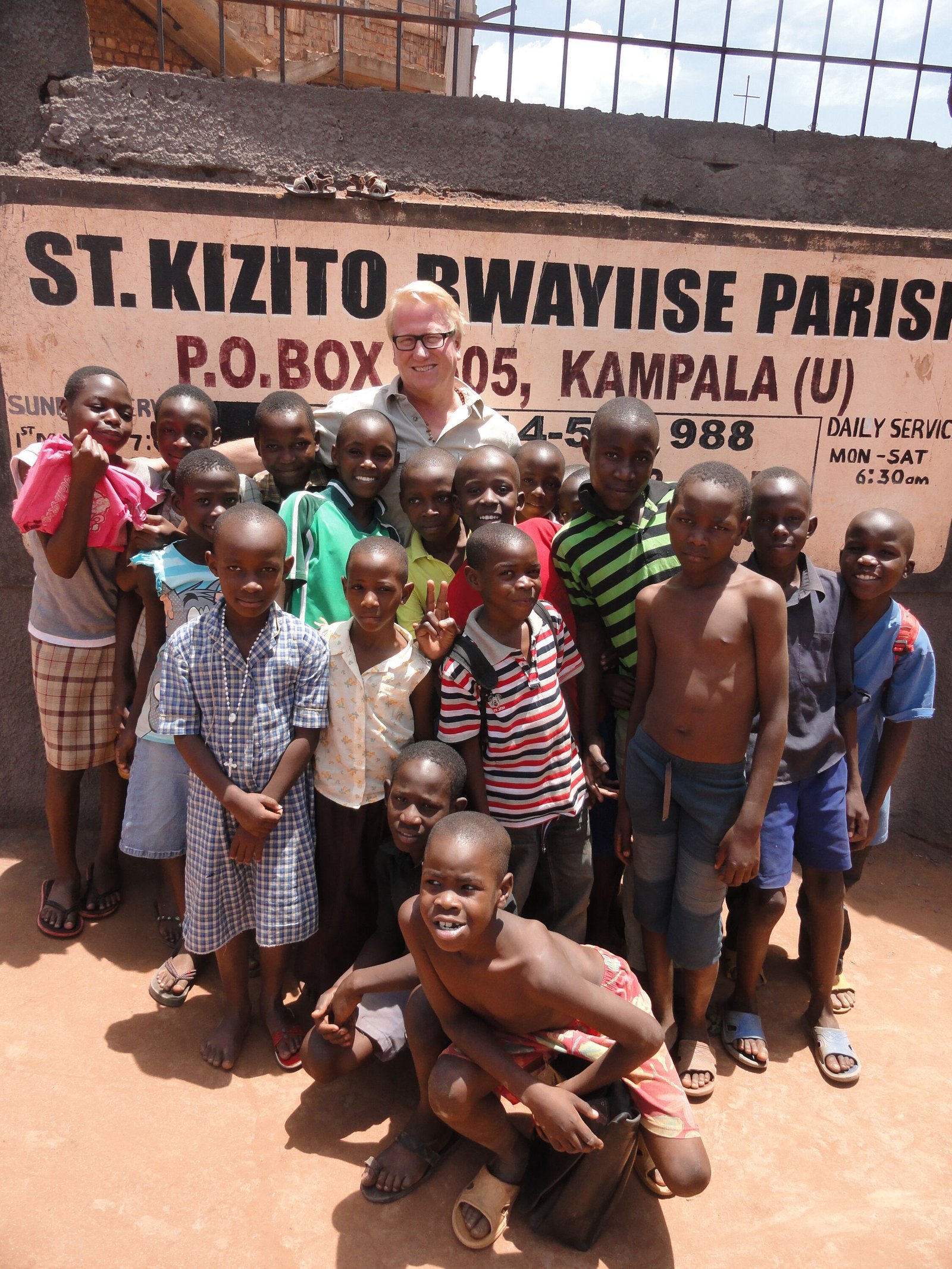 Our Lady of Good Counsel parishioner Bill Tulloch visits with neighborhood children at the gate outside St. Kizito Parish in Uganda.