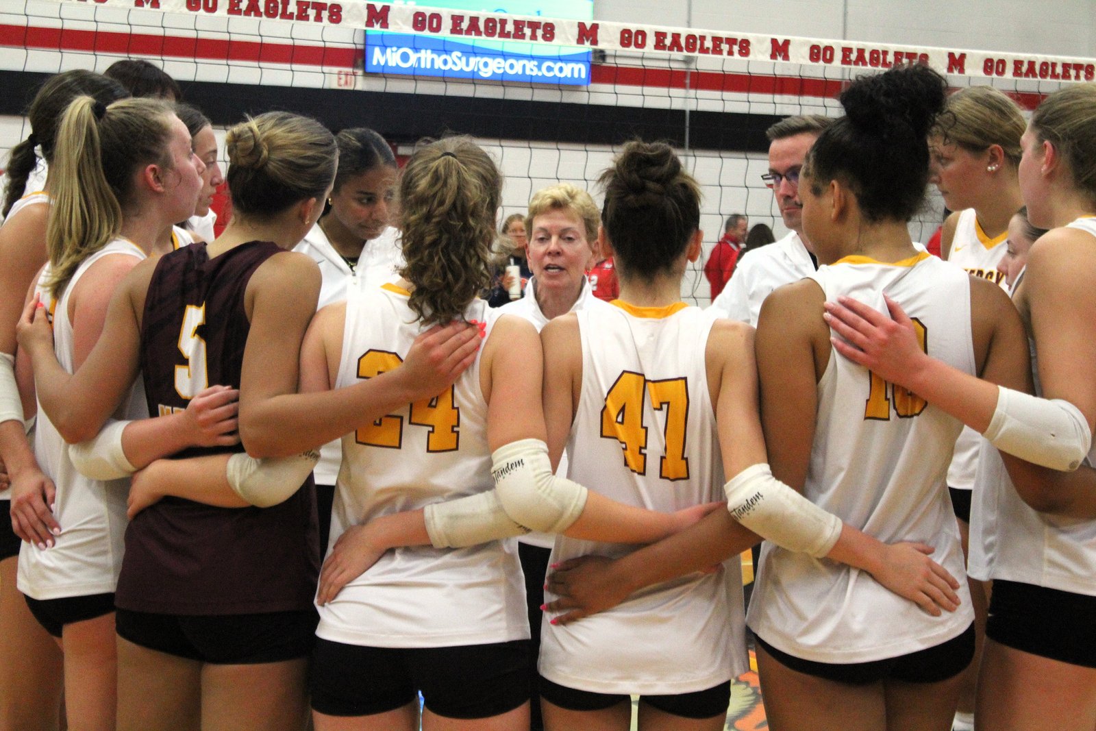 Mercy coach Loretta Vogel (center) is nearly dwarfed by her players in a between-set huddle. Nearly half of the players on the Marlins’ roster of 13 are 6 feet or taller.