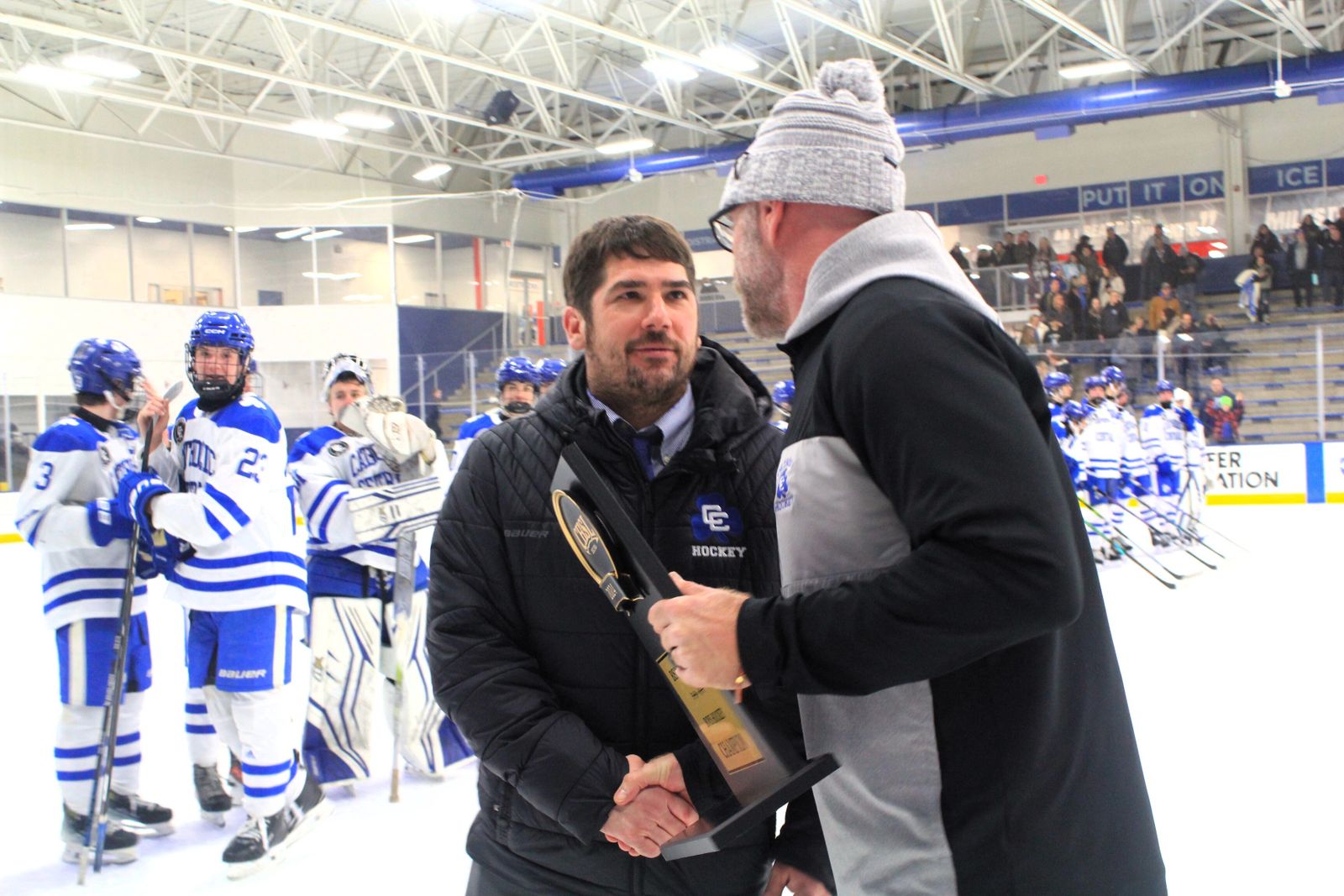 Catholic Central head coach Brandon Kaleniecki accepts the Catholic League hockey championship trophy from athletic director Aaron Babicz.