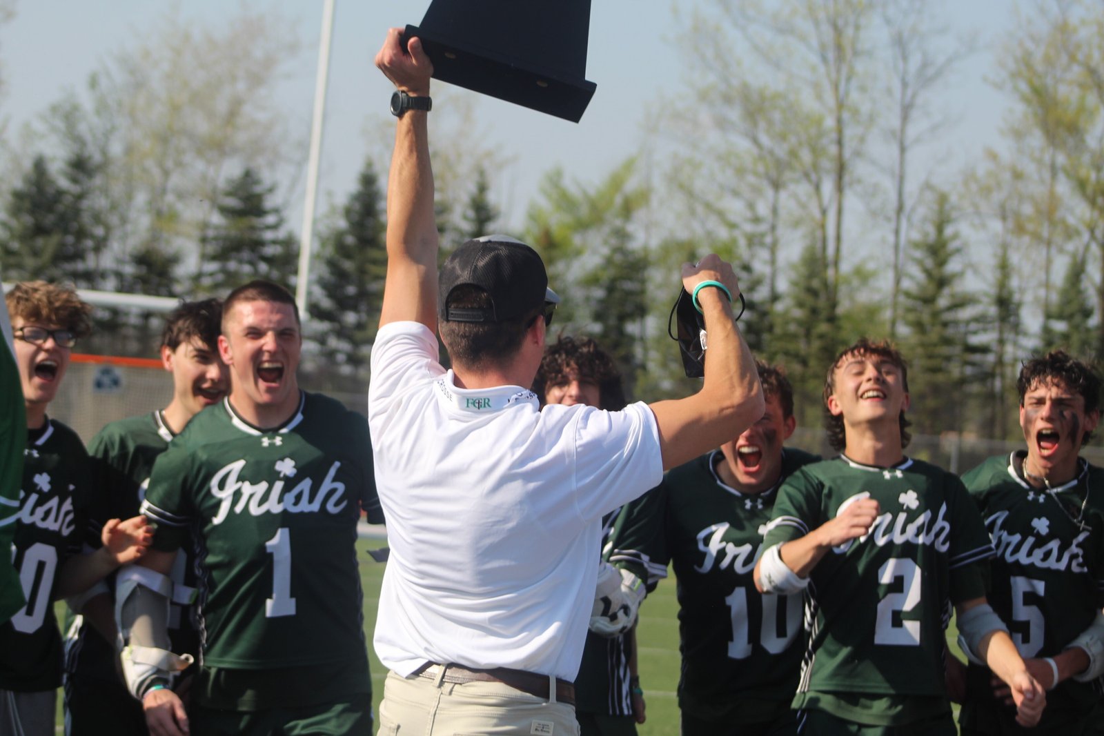 Head coach Joe Fitzgerald presents the Catholic League Cardinal Division lacrosse championship trophy to his joyous Ann Arbor Fr. Gabriel Richard team. It was the Fighting Irish’ first league title in eight seasons.